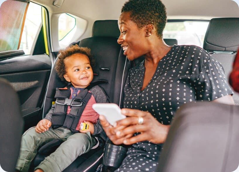 A parent and child riding in the back of a taxi, phone in hand.