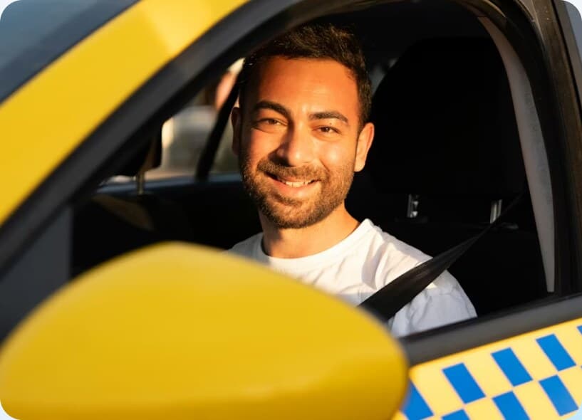 A driver at the wheel of a yellow cab, smiling.